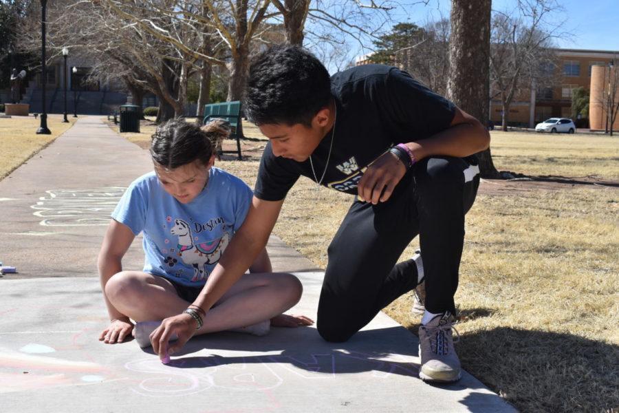 Senior physical education major, Carlos Carrillo, practices drawing with chalk in the Oval before the chalk art competition April 7. Carrillo was showing off a few tips and tricks to a friend’s sister, Karsyn Milanic. 