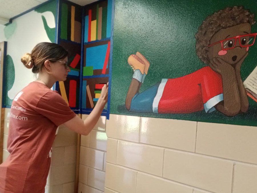 Abigail Buster completes the bookshelf portion of her mural in Gary Hall. This section, though small, will emphasize the theme of the entire project: “To Read is to Explore.”