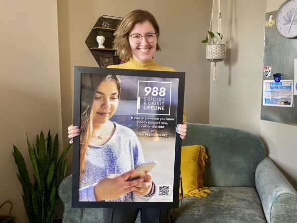 Rachel Drechsler holds a poster with details about the 988 hotline, which is a lifeline that students can call or text anytime of the day. 